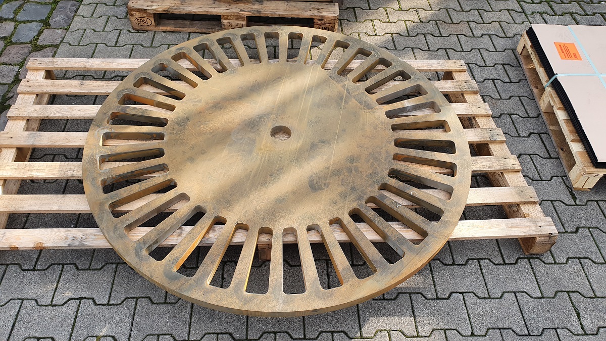 Runde Metallplatte mit Lüftungsschlitzen auf Holzpalette, Industriekomponente der Edelstahlverarbeitung.