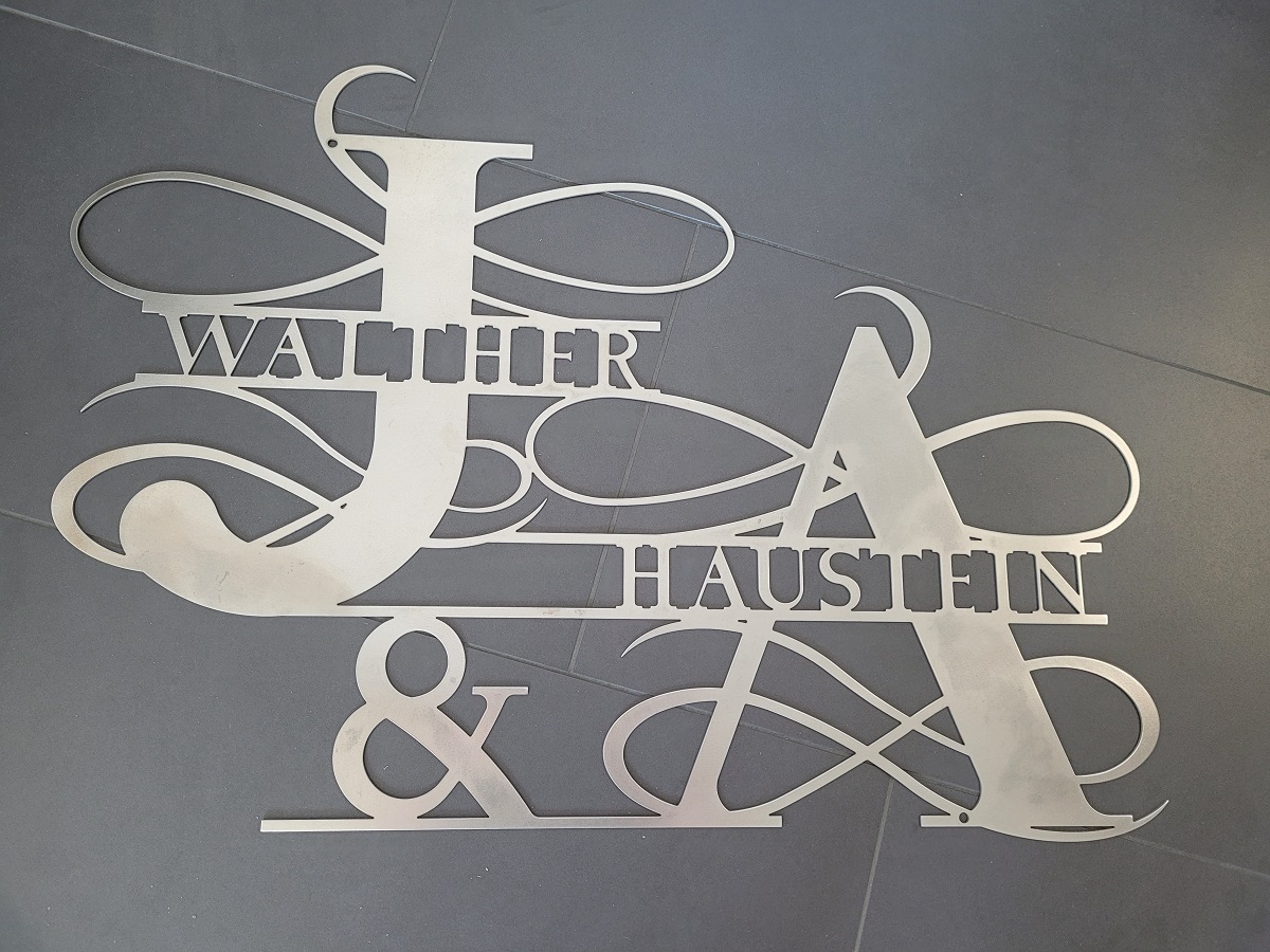Weißes Edelstahl-Logo mit Schriftzug Walther Haußstein & Co und verschlungenen Monogrammen auf grauem Hintergrund.