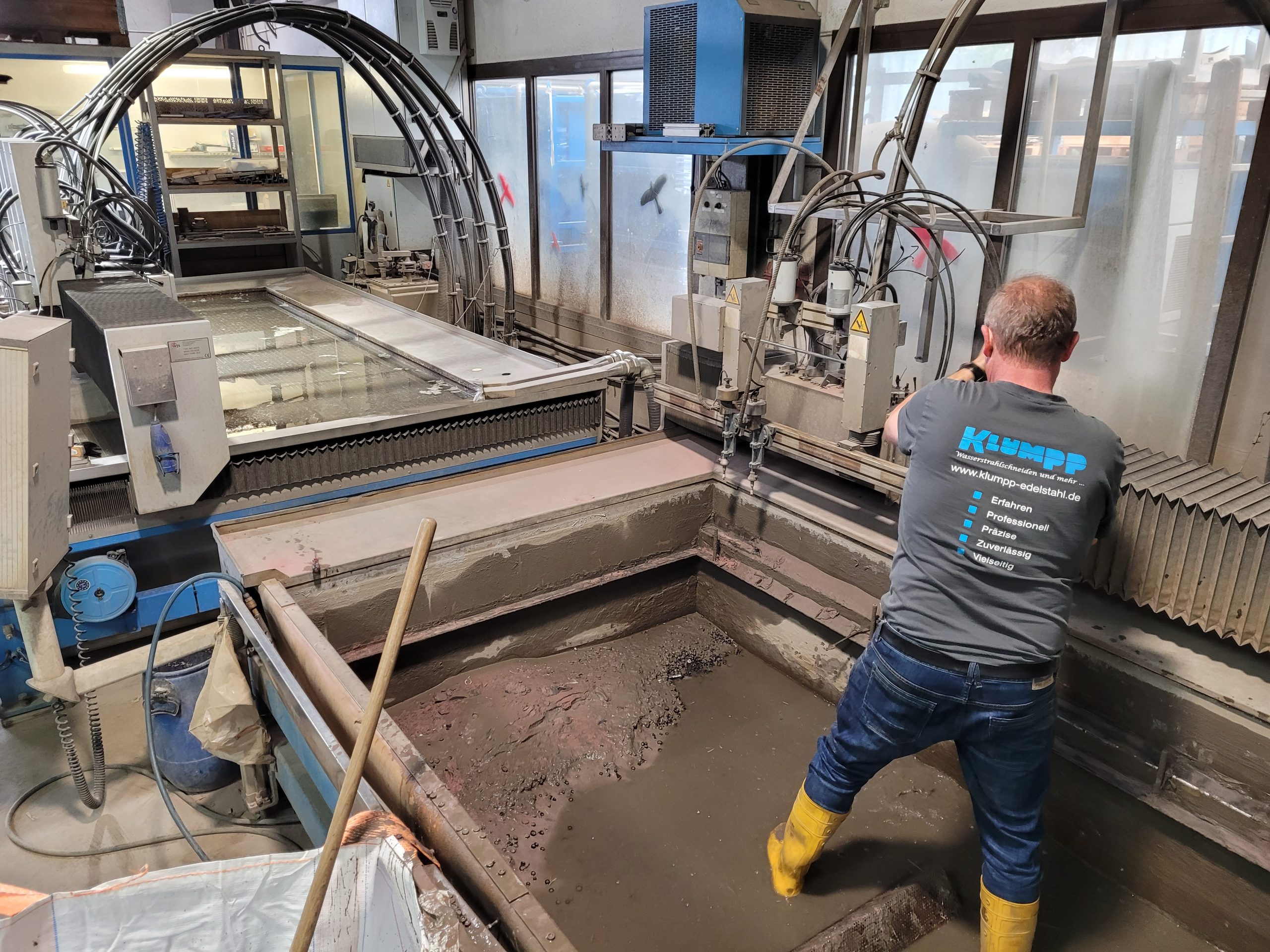 Mitarbeiter bei Klumpp überwacht Wasserstrahlschneidemaschine in Werkstatt mit Wasserbecken und Edelstahlausrüstung.