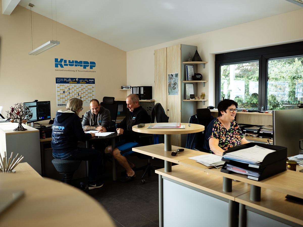 Klumpp-Büro in Altlußheim: Mitarbeiter bei Besprechung am runden Tisch, moderne Arbeitsräume mit Holzmöbeln und großen Fenstern.