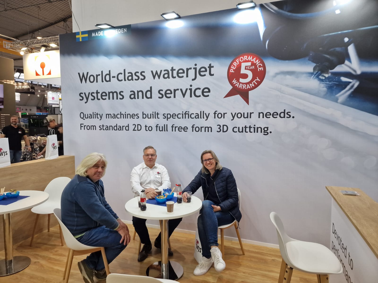 Drei Personen sitzen an einem Tisch auf der Messestand von Klumpp Wasserstrahlschneiden. Made in Sweden Banner mit 5-Jahres-Garantie sichtbar.