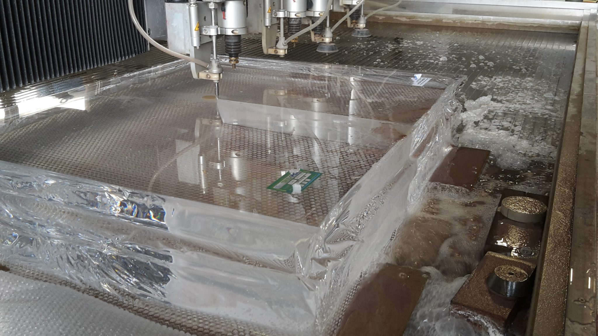 Edelstahl-Werkstück beim Wasserstrahlschneiden, Metallbearbeitung in industrieller Produktionshalle mit CNC-Maschine.