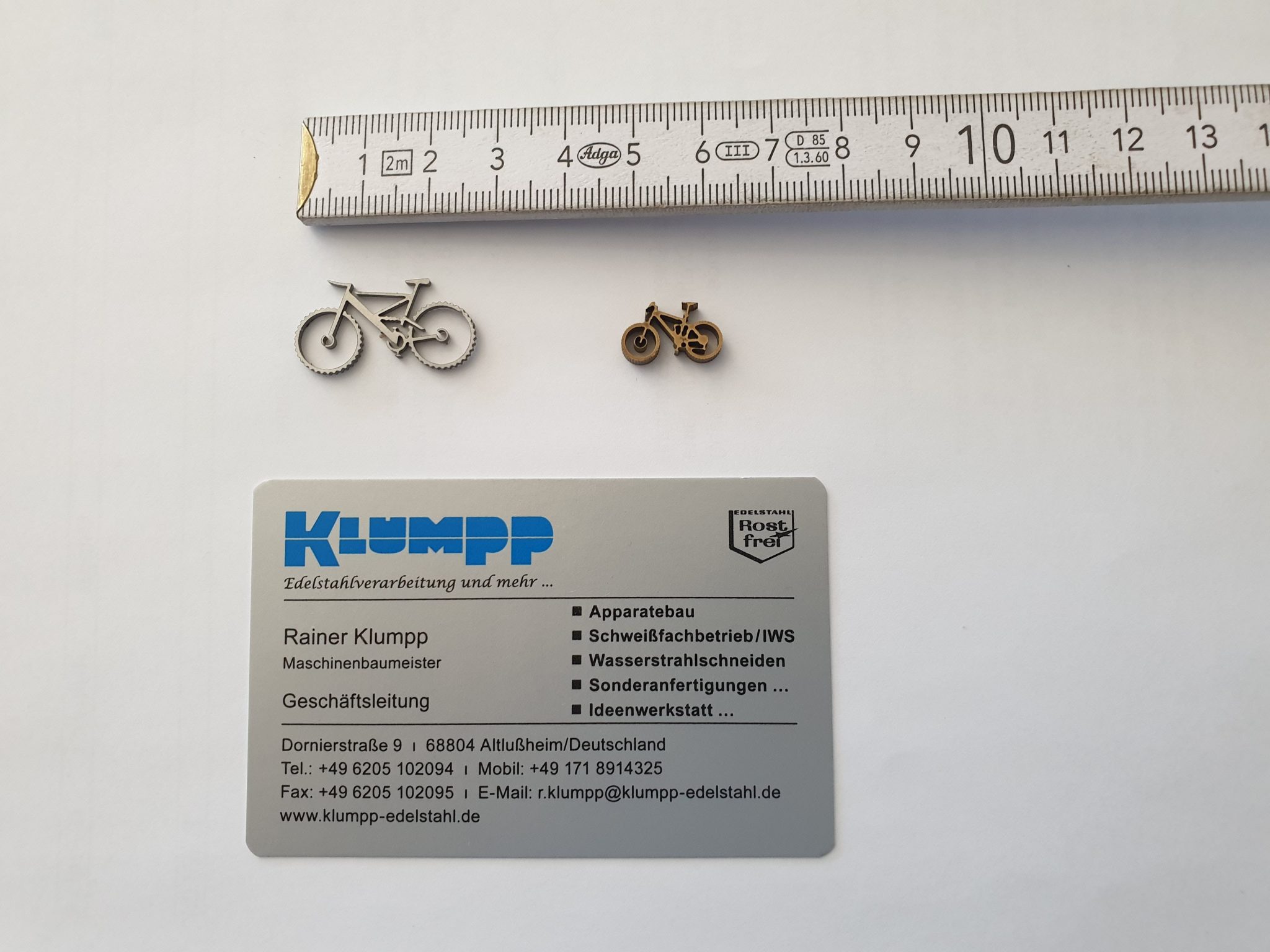 Zwei Edelstahl-Fahrrad-Miniaturen neben Maßstab und Visitenkarte von Klumpp Edelstahlverarbeitung Altlußheim.