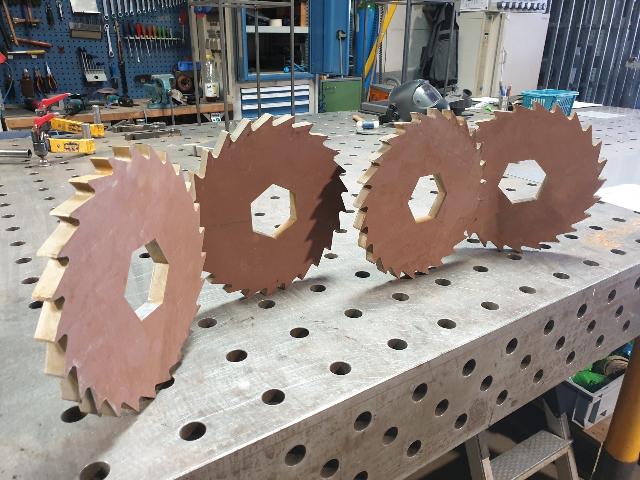 Drei Sägeblätter aus Metall mit Zähnen auf Werkbank in Industriewerkstatt mit Werkzeugen und Maschinen.