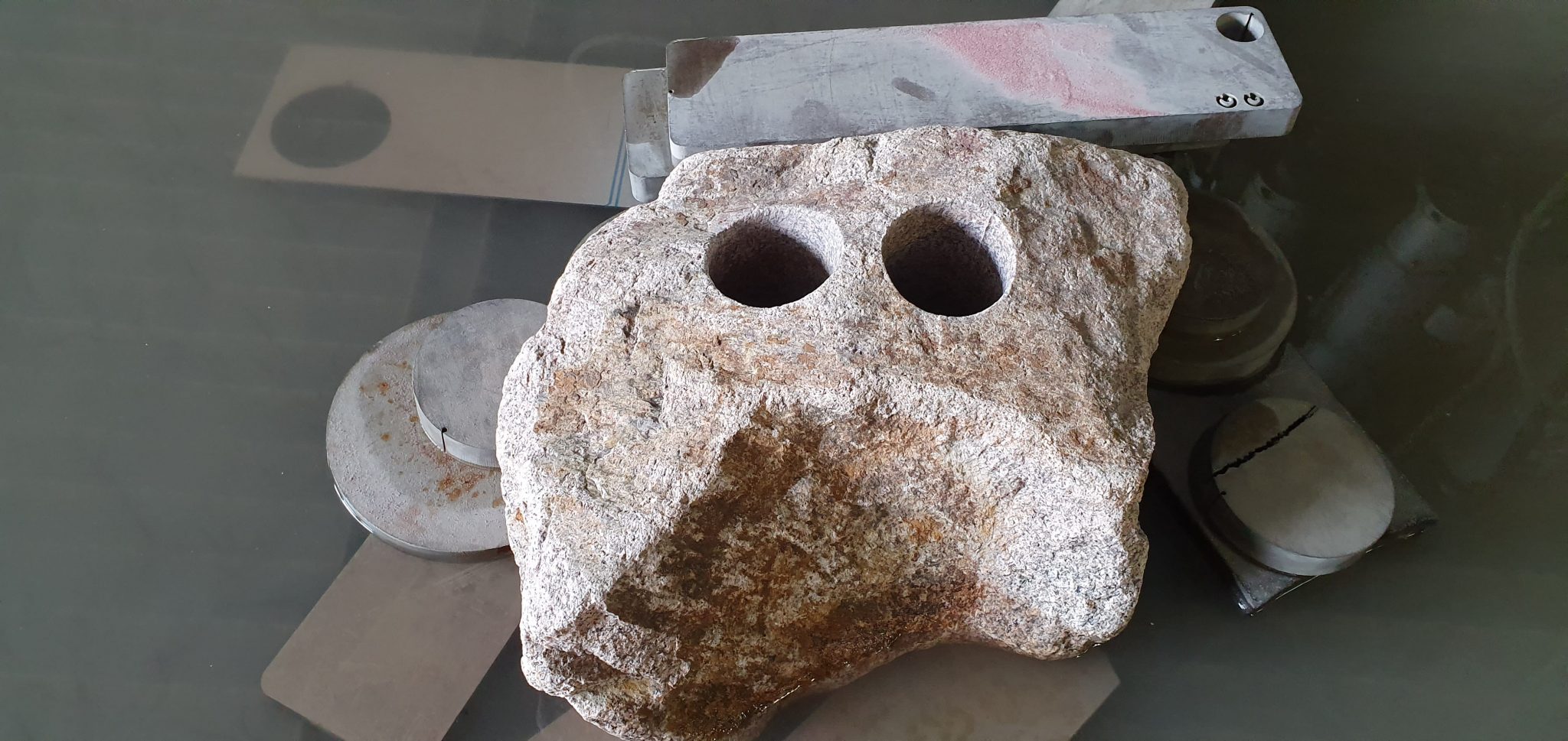 Poröser Werkstein mit zwei runden Bohrungen, daneben Stahllineal zur Größenreferenz bei Wasserstrahlschneiden-Bearbeitung.