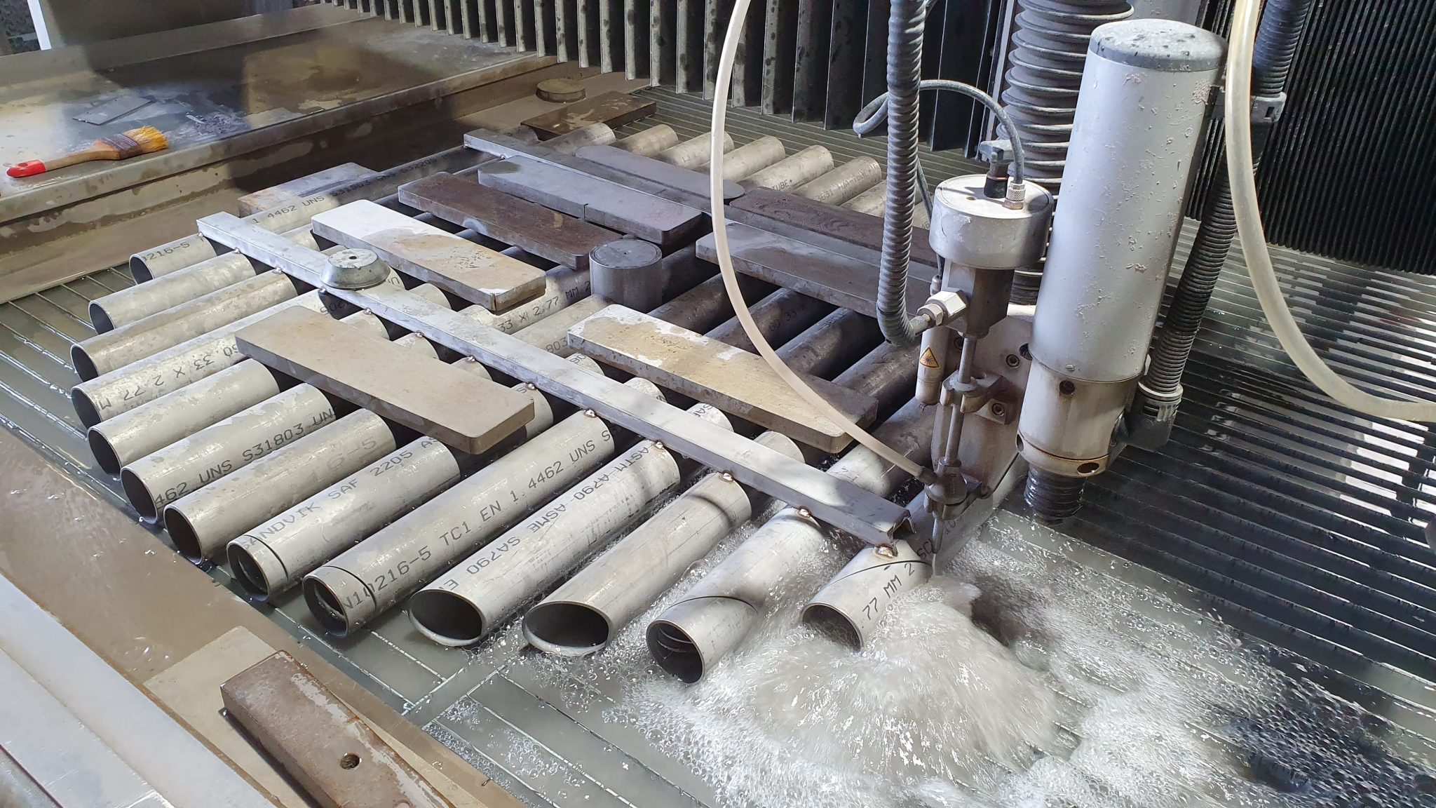 Wassergesnittene Edelstahlrohre und -platten auf Werkbank mit Schneidemaschine bei Klumpp Wasserstrahlschneiden Altlußheim.