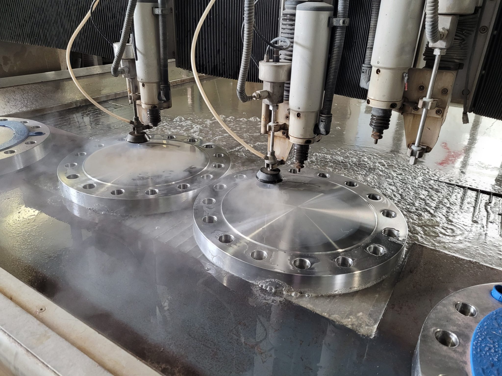 Wasserstrahldüsen schneiden präzise Edelstahlflanschen mit Bohrungen. Industrielle CNC-Bearbeitung bei Klumpp Altlußheim.