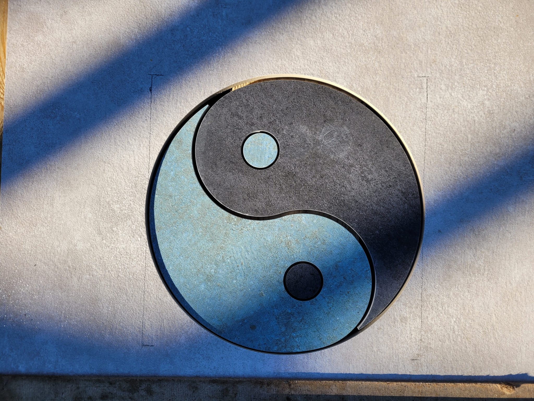 Yin-Yang Symbol aus Edelstahl in Blau und Grau auf heller Wand, geschnitten mit Wasserstrahlverfahren, zeigt Handwerkskunst.