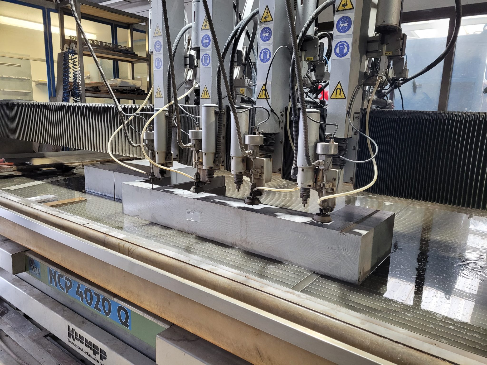 Klumpp Wasserstrahlschneidmaschine NCP 4020 Q schneidet Edelstahlblock präzise in Werkstatt mit Sicherheitsmarkierungen.