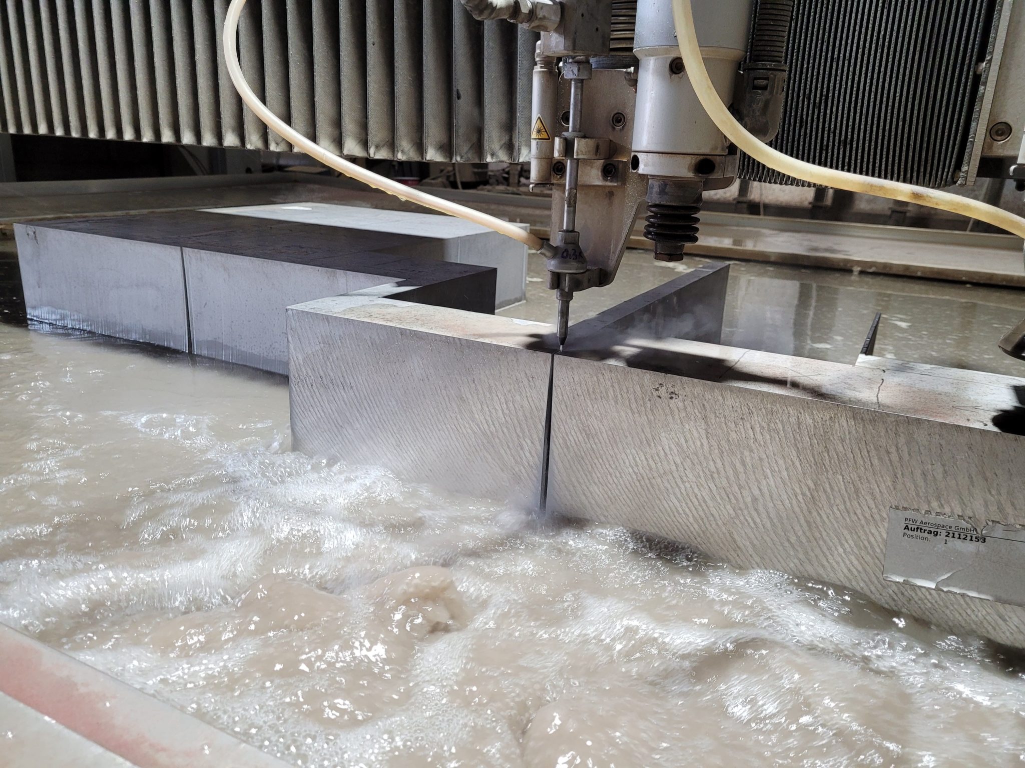 Wasserstrahlschneidemaschine schneidet Edelstahlplatte präzise in Werkstatt mit Wasserbad und industriellen Anlagen.