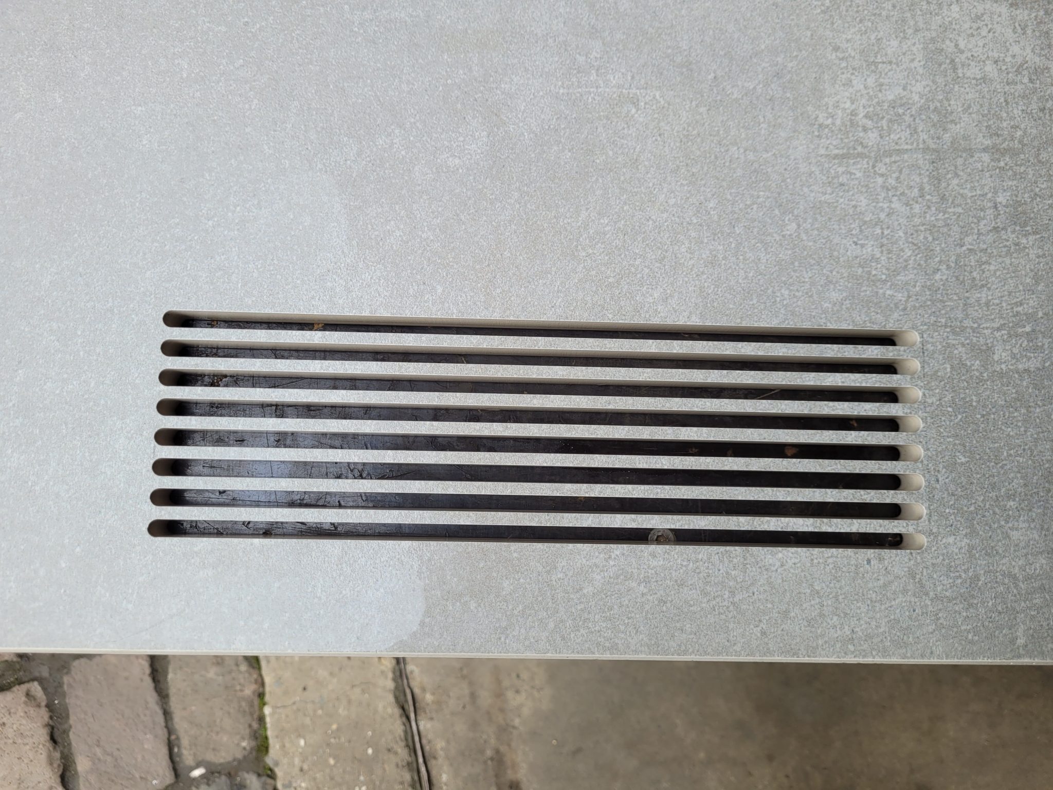 Neun parallele Edelstahlstäbe mit gerundeten Enden auf grauem Untergrund, handwerklich gefertigt durch Wasserstrahlschneiden.