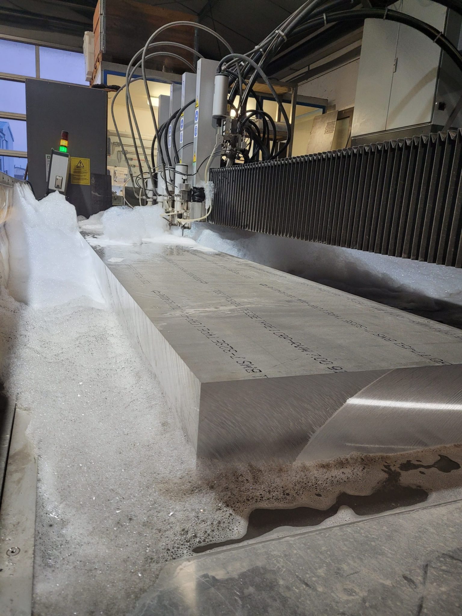 Wasserstrahlschneidemaschine schneidet Edelstahlplatte mit Präzision in Produktionshalle, Metallspäne sichtbar.
