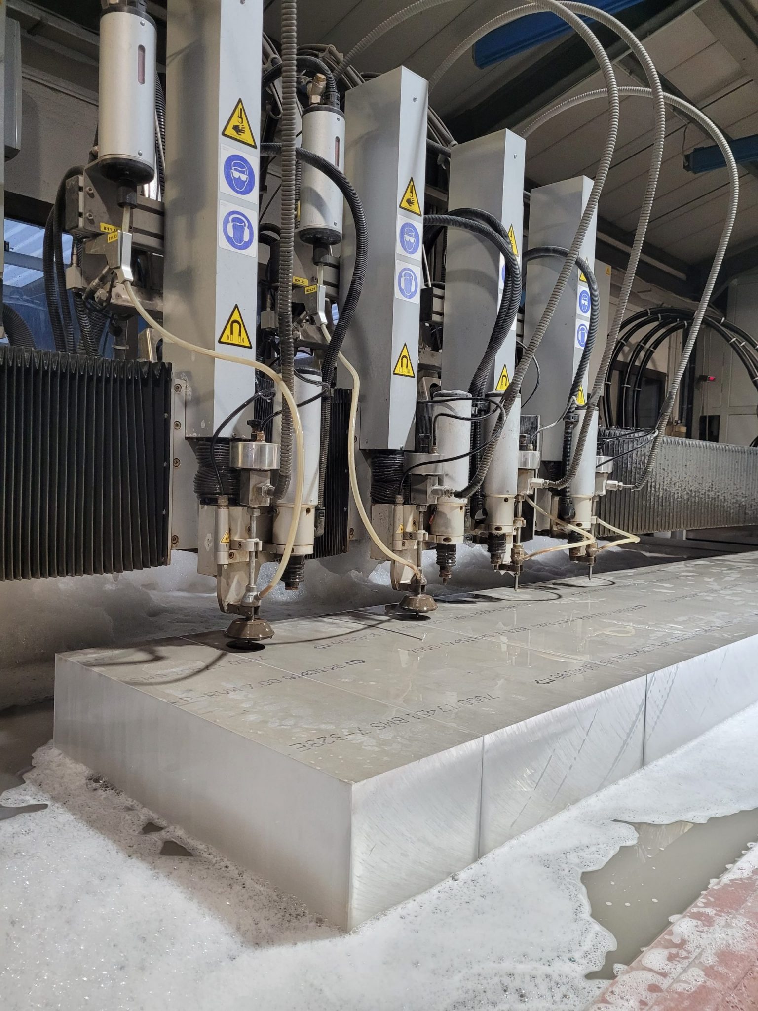 Wasserstrahlschneidanlage mit vier weißen Schneidköpfen in modernem Industriegebäude bei Klumpp Edelstahlverarbeitung.