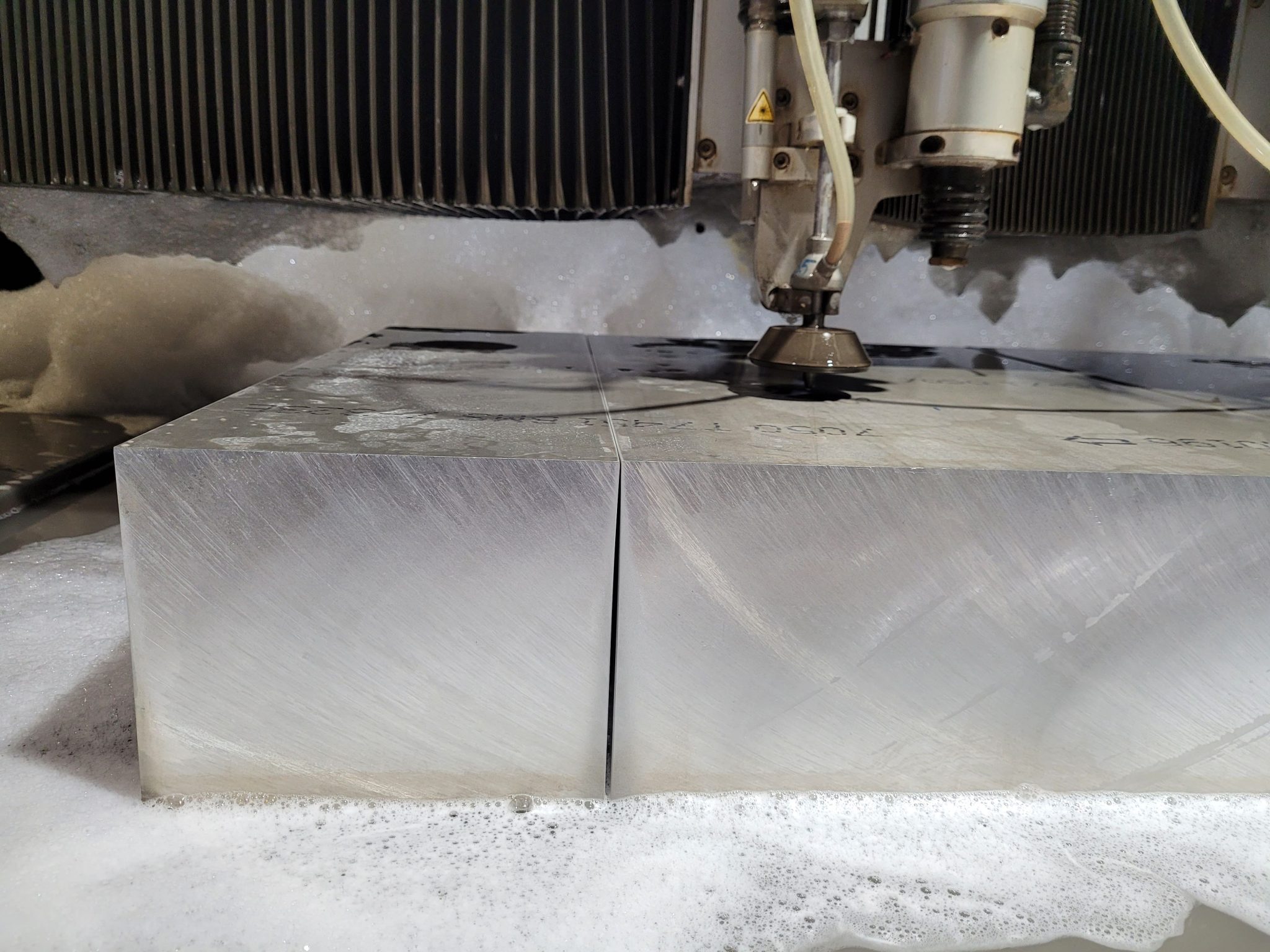 Wasserstrahlschnitt durch Edelstahlblock, Schneidekopf mit Wasserstrahldüse, Schaumabfall, industrielle Präzisionsbearbeitung
