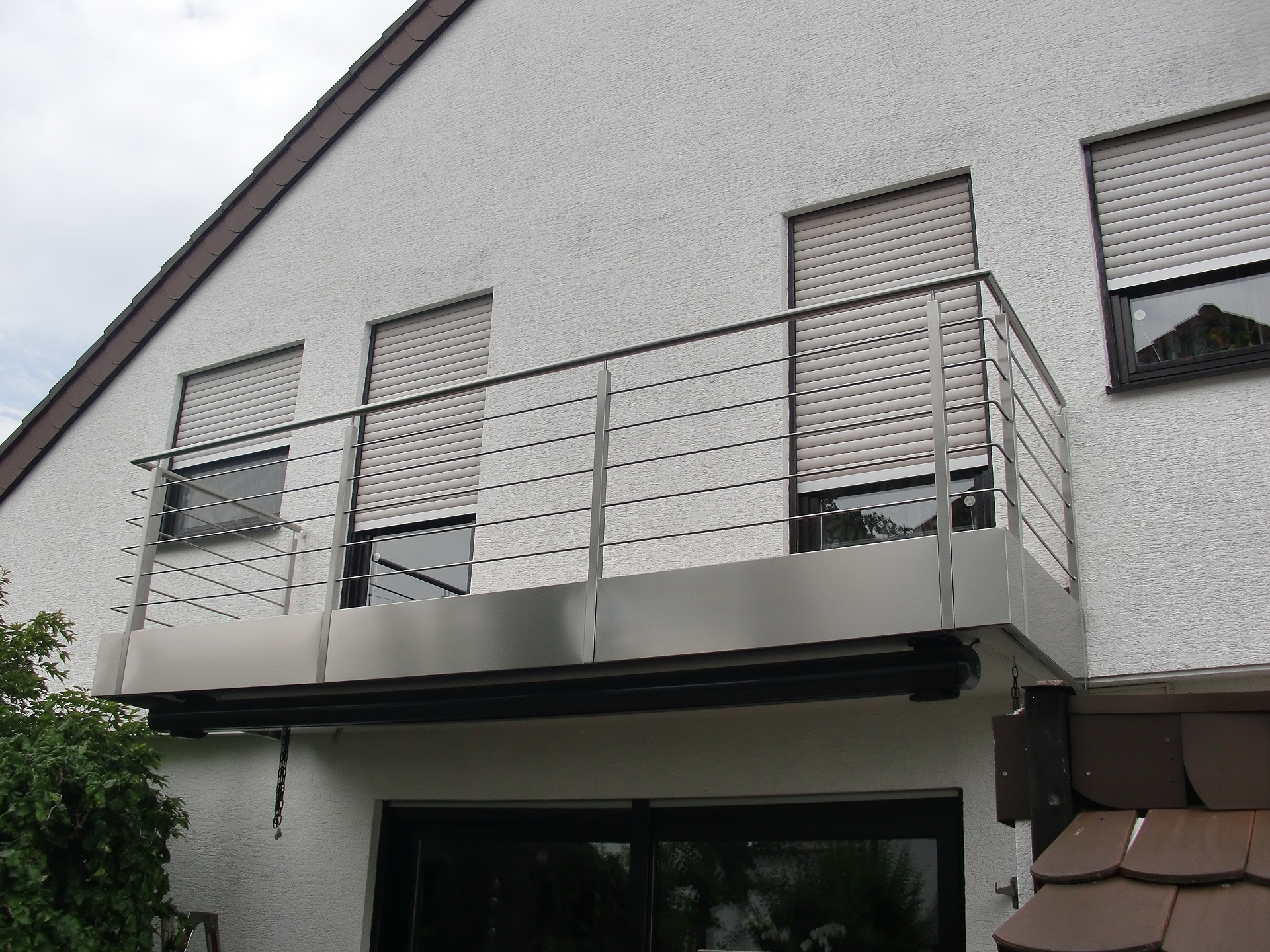 Moderne Edelstahl-Balkongeländer an Wohnhaus mit horizontalen Stäben und matter Oberfläche, hochwertige Verarbeitung.