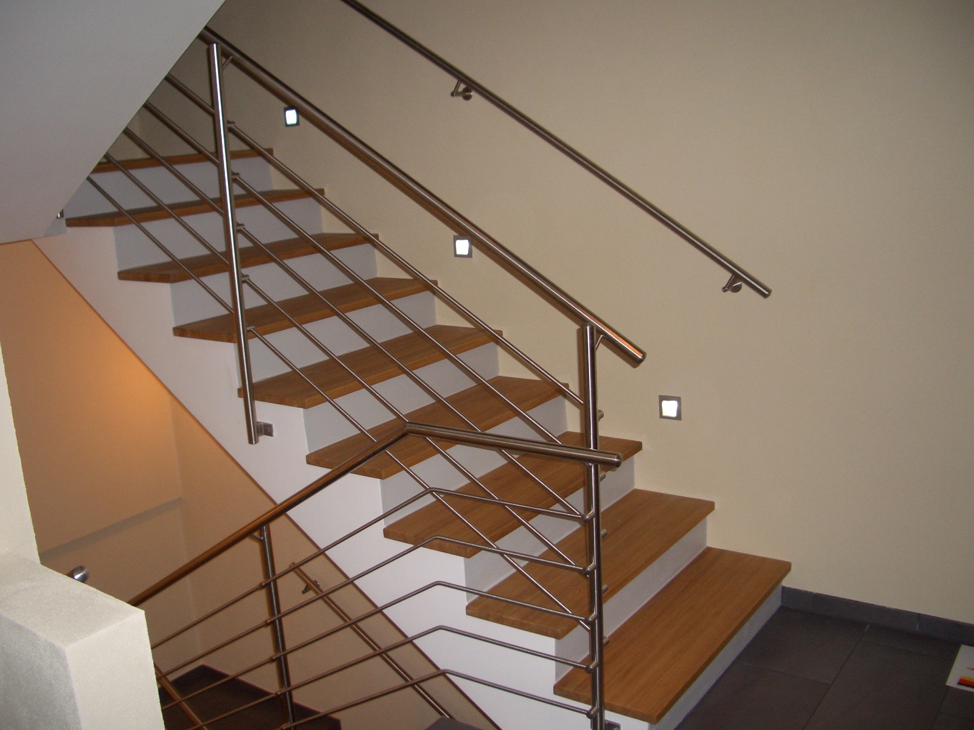 Moderne Treppe mit Holzstufen und Edelstahl-Geländer mit Querstreben, indirekte Beleuchtung an der Wand, helles Treppenhaus.