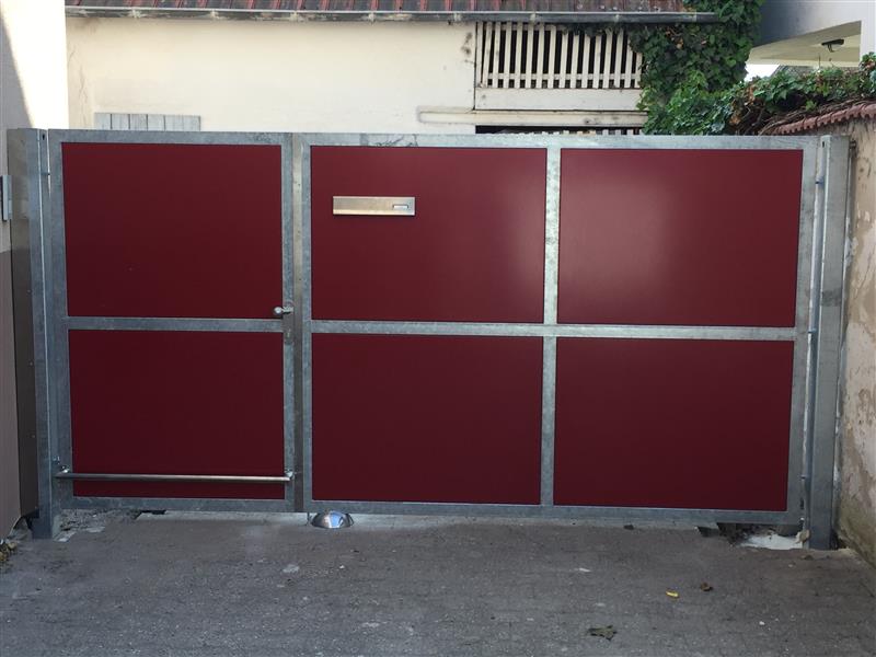 Rote Metalltor mit Edelstahlrahmen, modernes Hoftor mit Briefkasten, geschlossenes Einfahrtstor vor Wohnhaus.