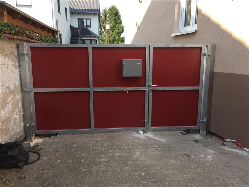 Rote Stahltor mit Metallrahmen und Intercom-System vor Wohnhaus, modernes Einfahrtstor für private Zufahrt.