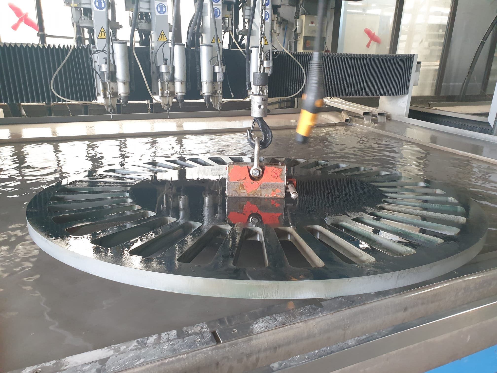 Wasserstrahlschneidemaschine schneidet Edelstahlblech mit Hochdruckwasserstrahl auf Rundtisch in Werkstatt.