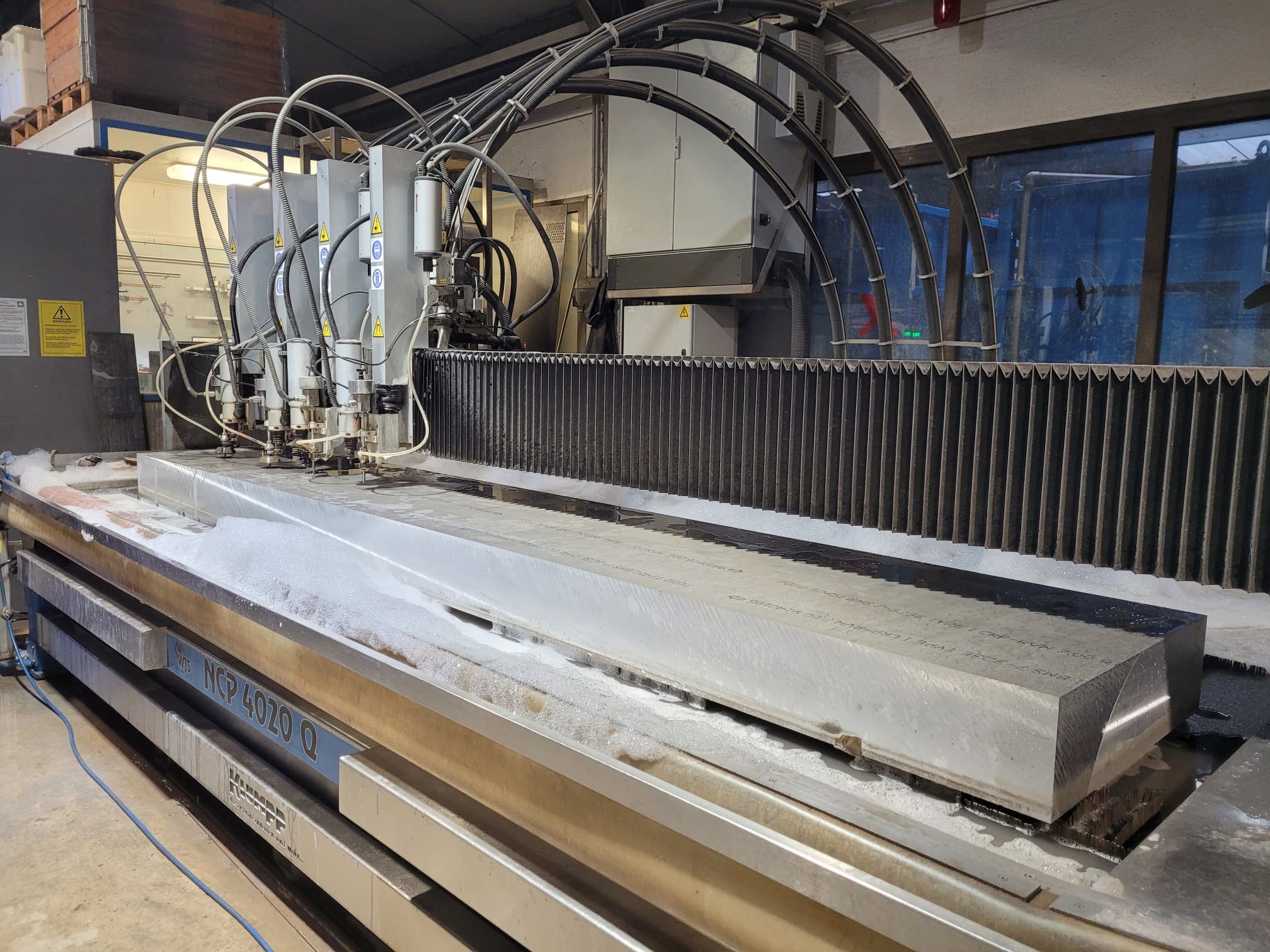 Wasserstrahlschneidemaschine mit Edelstahlplatte, Hochdrucksystem und Schneidekopf in Werkstatt.