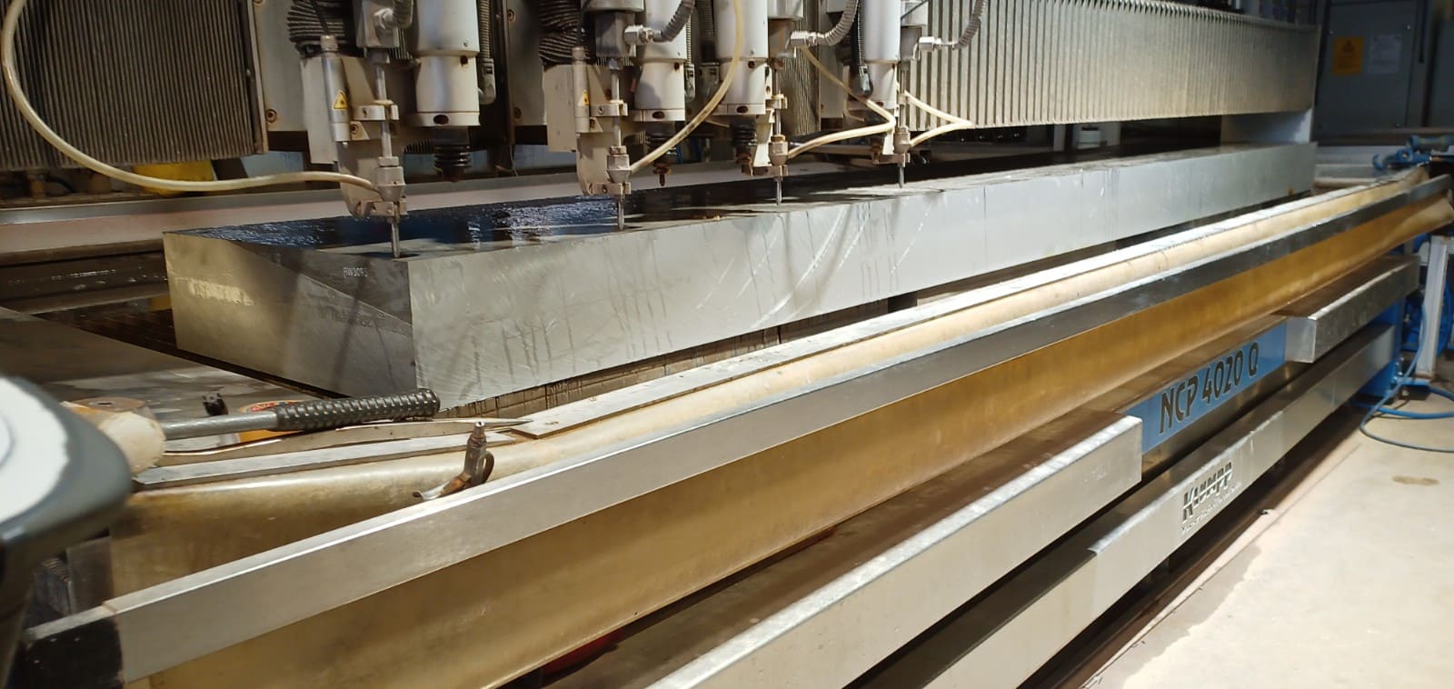 Wasserstrahlschneidanlage mit Edelstahlwerkstück, Schneidköpfe präzisionieren Metallplatte in modernem Produktionsbetrieb.