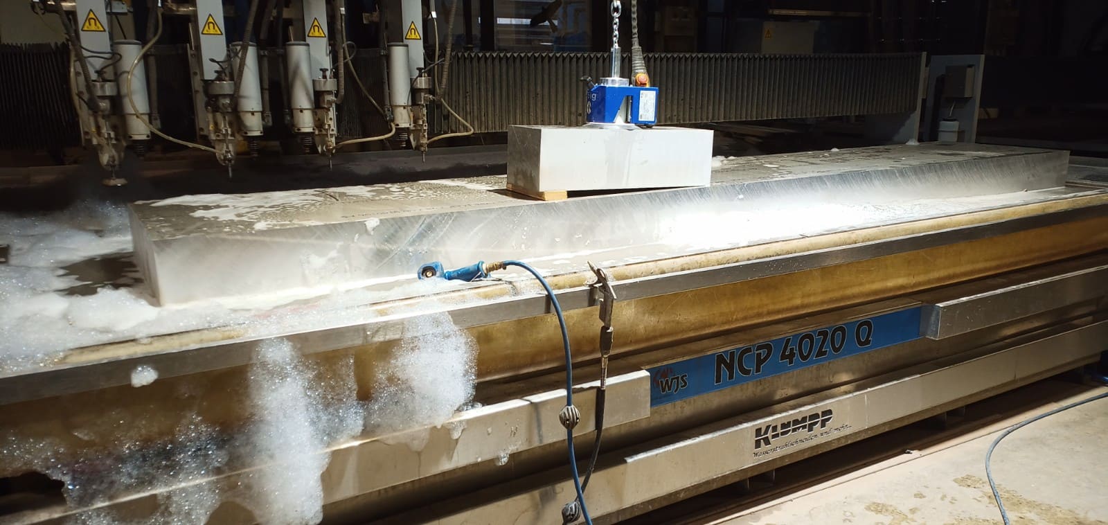 Wasserstrahlschneidanlage NCP 4020 C beim Schneiden von Edelstahlplatte in Industriehalle mit Wasserdampf und Schleifmittelanlage.