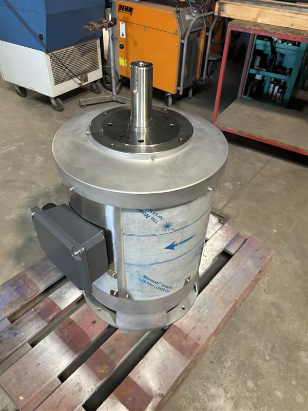 Edelstahl-Hydraulikmotor auf Holzpalette in Werkstatt mit Maschinen im Hintergrund.