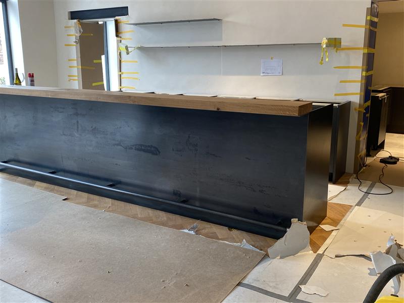 Moderne Ladentheke aus Edelstahl und Holz in Baustelle, gelbe Schutzvorrichtungen, professionelle Handwerksumsetzung bei Klumpp Edelstahlverarbeitung.