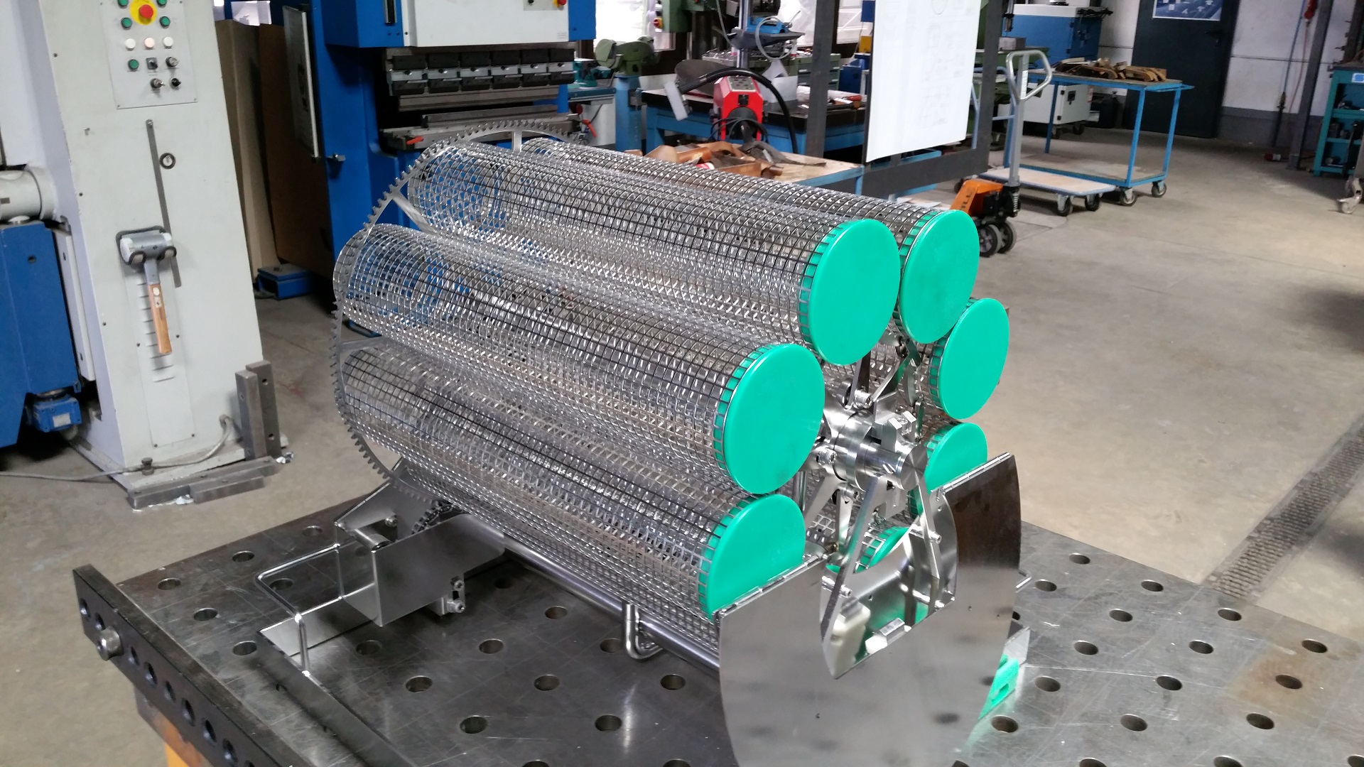 Edelstahl-Siebwalze mit grünen Endscheiben auf Werkstattplattform in Industriehalle mit Maschinen.