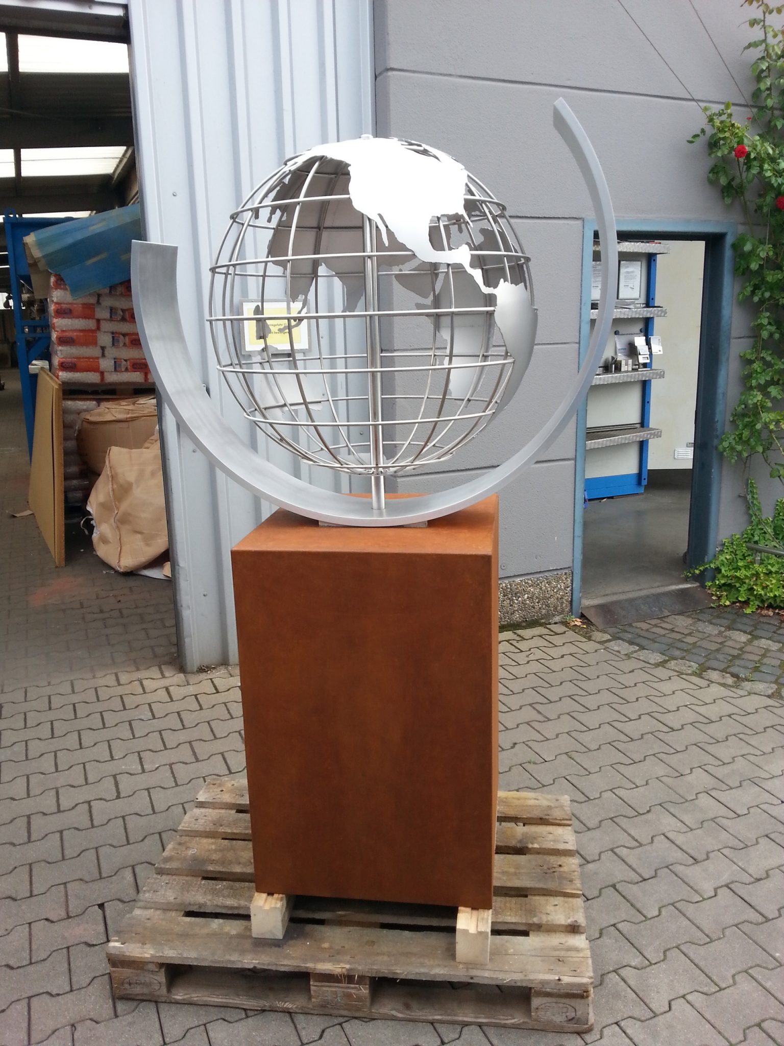 Globus-Kunstobjekt aus Edelstahl auf rotem Sockel vor Industriegebäude, Klumpp Edelstahlverarbeitung Altlußheim.