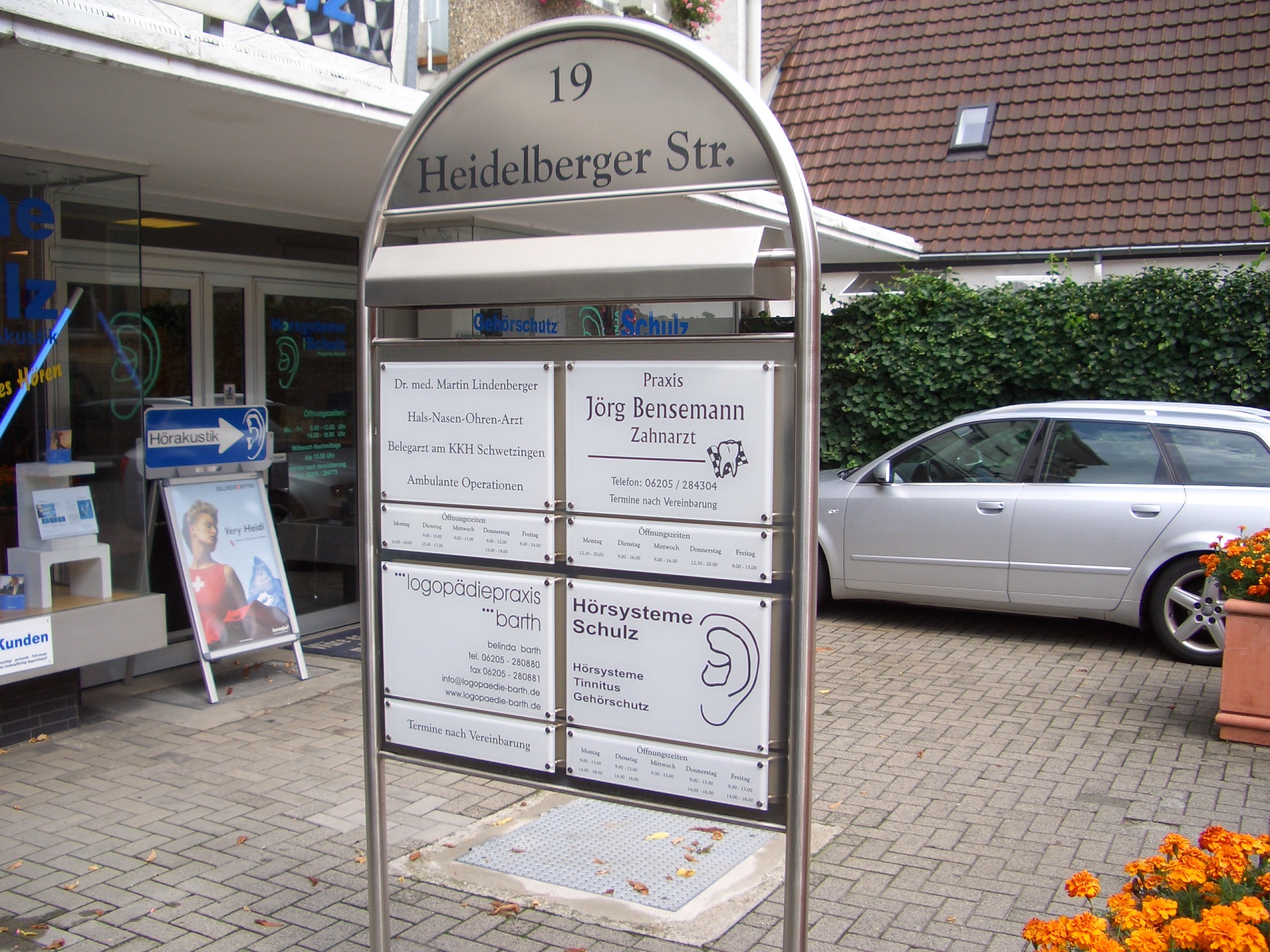 Straßenschild 19 Heidelberger Str. mit Praxisschildern für Zahnarzt und Hörsysteme an Geschäftshaus in Altlußheim.