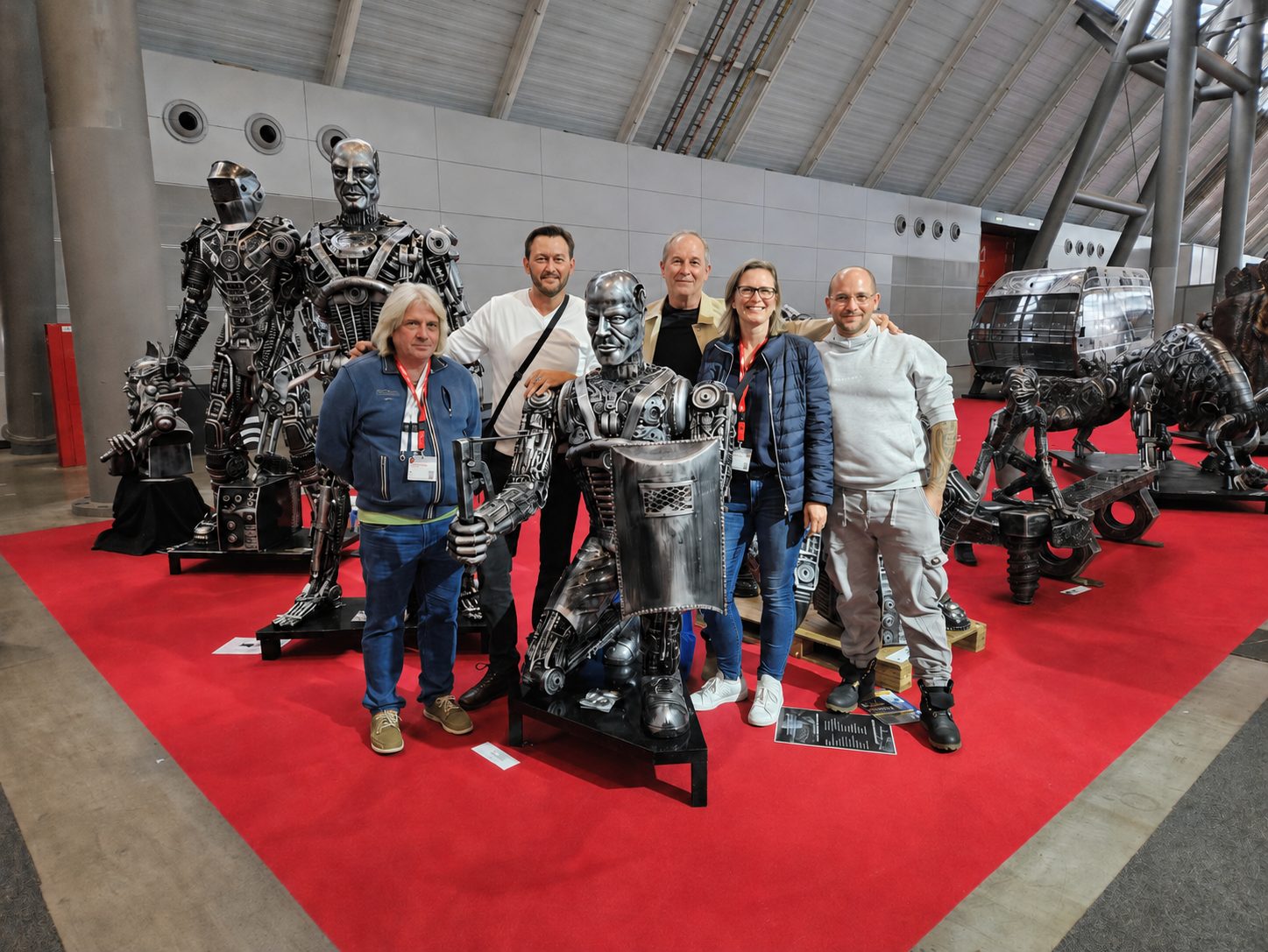 Das Klumpp-Team vor metallischen Roboter- und Maschinenskulpturen in einer Industriehalle mit rotem Teppich.